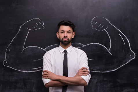 Man met opgerolde mauwen en armen over elkaar met krijtbordtekening op achtergrond van spierballen