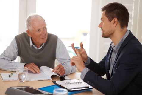 Foto jonge man die oudere man advies geeft met dossiers op tafel