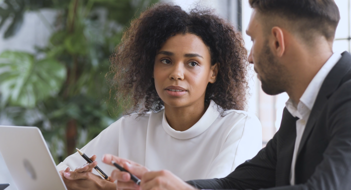 Een vrouw en man zitten achter een laptop in discussie