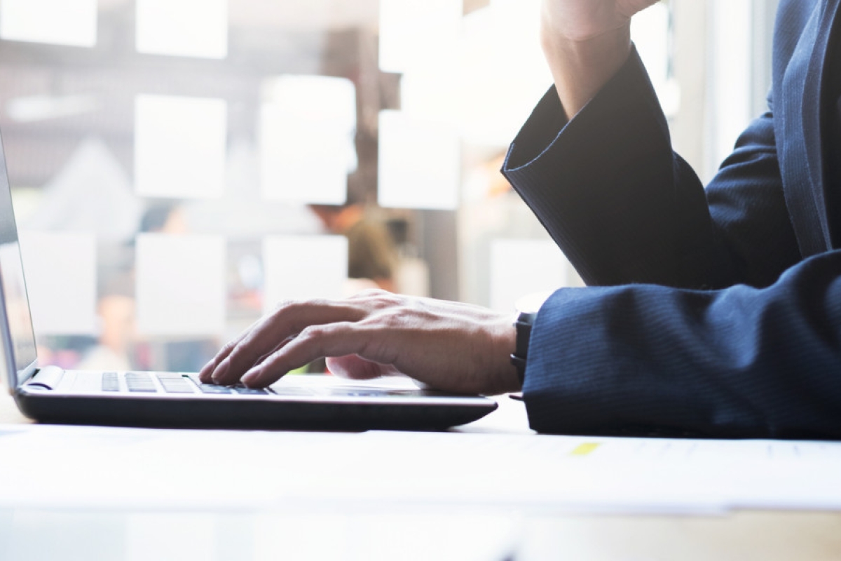 Een uitsnede van de torso van iemand die in een kantooromgeving achter een laptop zit te werken.