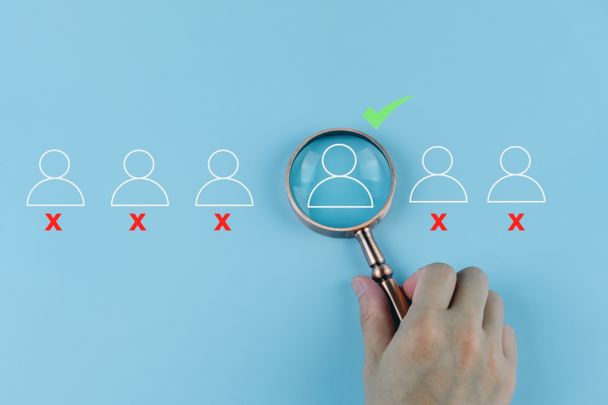 Poppetjes op een rij waarvan 1 met een groen vinkje onder een vergrootglas.