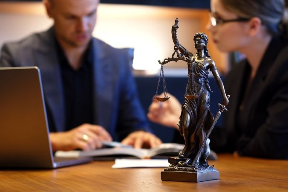 Beeldje vrouwe justitia met in de achtergrond twee personen aan tafel