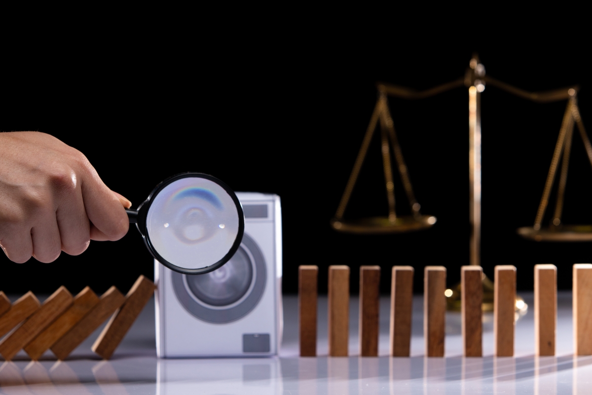 kleine wasmachine met daarvoor een hand met vergrootglas, op achtergrond weegschaal