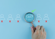 Poppetjes op een rij waarvan 1 met een groen vinkje onder een vergrootglas.