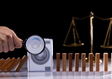 kleine wasmachine met daarvoor een hand met vergrootglas, op achtergrond weegschaal