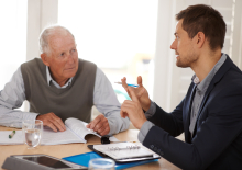 Foto jonge man die oudere man advies geeft met dossiers op tafel