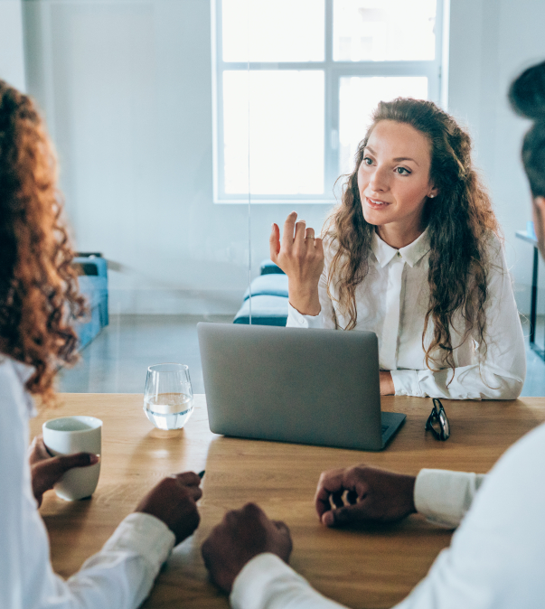 Een vrouw met laptop in gesprek met man & vrouw aan vergadertafel