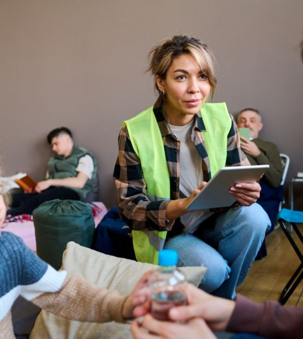 Vrouw in hesje met klembord helpt mensen in een opvangcentrum